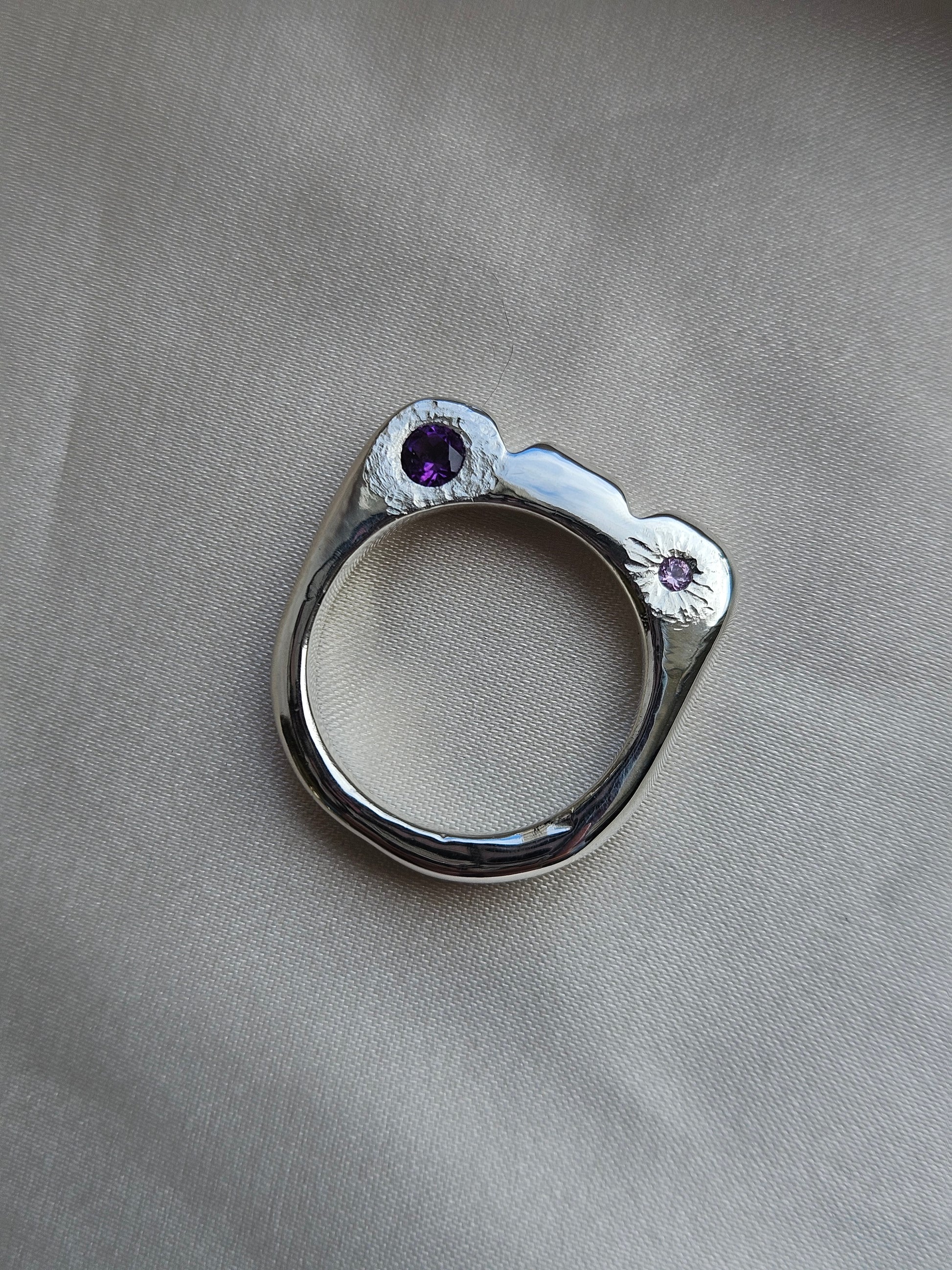 Silver ring with purple gemstones on a gray fabric background