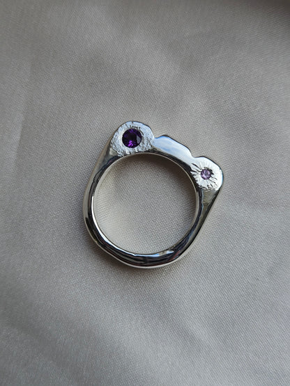 Silver ring with purple gemstones on a gray fabric background