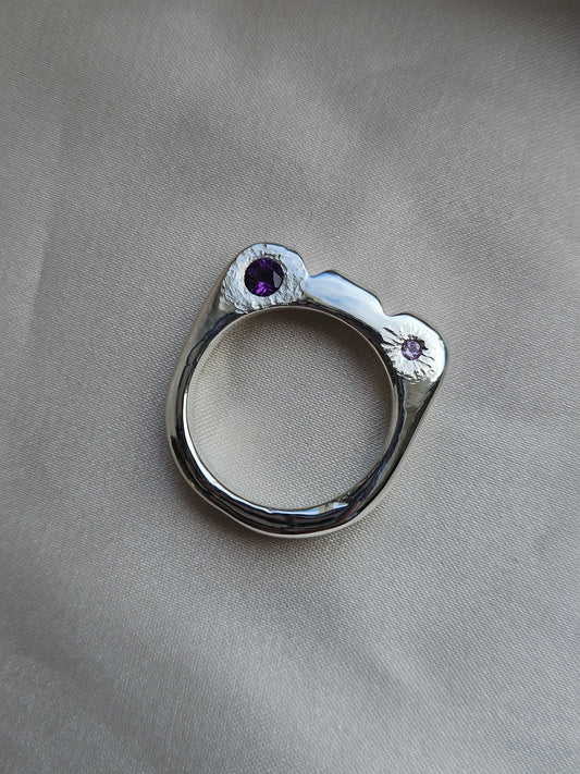 Silver ring with purple gemstones on a gray fabric background