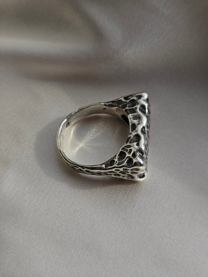 Silver ring with textured design on a gray fabric background