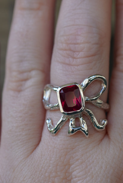 Silver ring in shape of bow with a red gemstone on a finger