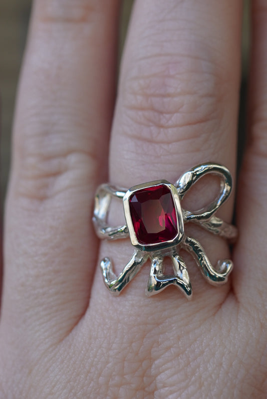 Silver ring in shape of bow with a red gemstone on a finger